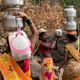 A woman helps another in carrying metal pitchers filled with water